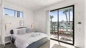 Een moderne slaapkamer met een groot bed, nachtkastjes, een raam met zonwering en uitzicht op de omgeving.