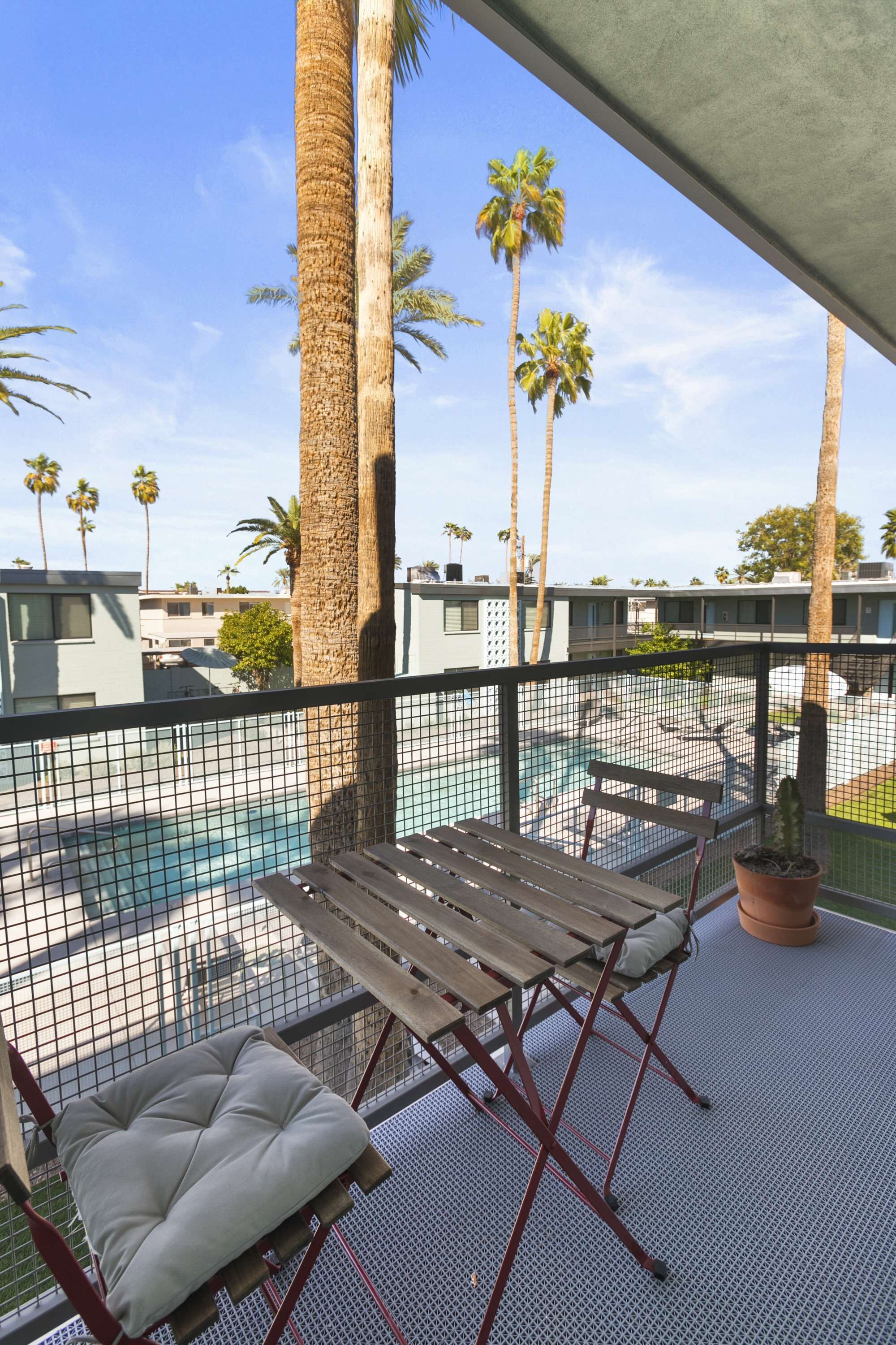 A balcony with a pool, palm trees, and a wooden bench.
