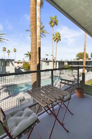 A balcony with a pool, palm trees, and a wooden bench.