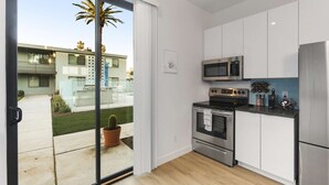 A modern kitchen with stainless steel appliances, a sliding glass door leading to a patio with a cactus, and a view of a residential building. - Poolside studio with rooftop deck (Scottsdale)