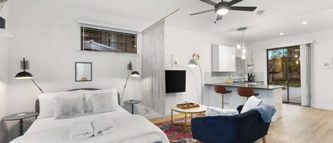 A modern bedroom with a bed, a blue armchair, a desk, and a ceiling fan.