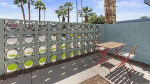 A patio with a wooden table and red chairs, a decorative fence with circular cutouts, and palm trees in the background. - Poolside studio with rooftop deck (Scottsdale)