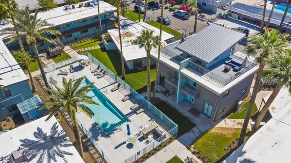 Un edifici modern amb una piscina al terrat, envoltat de palmeres i una zona d'aparcament.