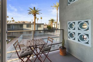 A balcony with a table and chairs, a potted plant, and a view of palm trees and buildings. - Micro studio with balcony, pool view, and rooftop (Scottsdale)