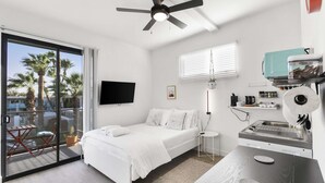 A modern hotel room with a bed, a TV, a ceiling fan, a kitchenette, and a balcony with a view of palm trees. - Scottsdale classic BoHo micro studio (Scottsdale)