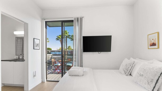 A hotel room with a bed, a TV, a balcony with a view of palm trees and a construction site, and a kitchenette. - Scottsdale classic BoHo micro studio (Scottsdale)