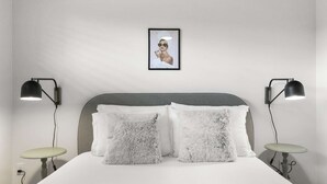 Ein ordentlich bezogenes Bett mit flauschigen Kissen, zwei Nachttischlampen und einem gerahmten Bild an der Wand.