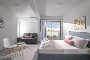 Una habitación de hotel moderna con cama, sofá, sillón, una mesita y un balcón con vistas.