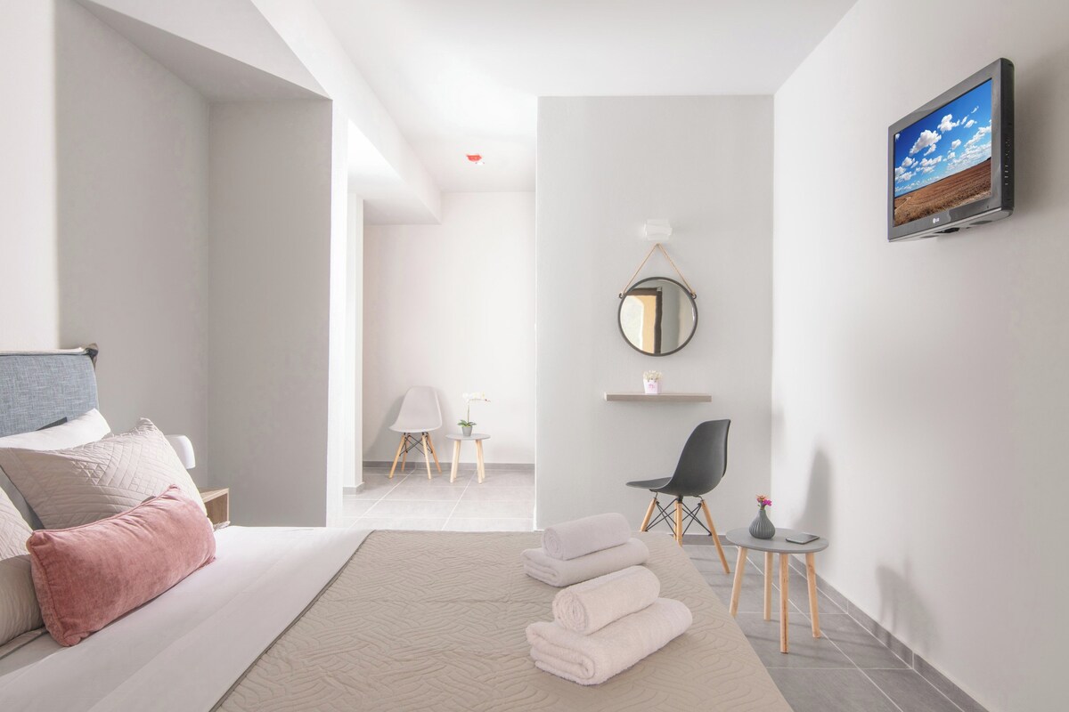 A modern hotel room with a bed, a flat-screen TV, a round mirror, and a small table with a vase.