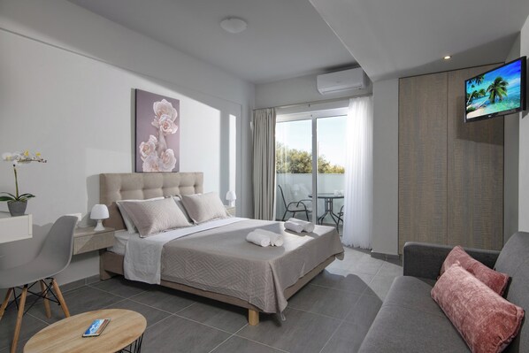 Une chambre d’hôtel moderne dotée d’un grand lit, d’une télévision à écran plat, d’un balcon avec vue et d’un coin salon comprenant un canapé et un fauteuil.