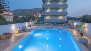 A modern building with a rooftop pool, outdoor seating, and a view of a mountain.