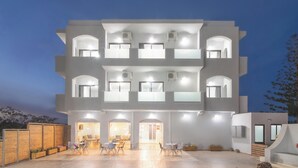 Un edificio de varios pisos con techo plano, ventanas grandes y un patio con mesas al aire libre.