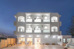 Un edificio de varios pisos con techo plano, ventanas grandes y un patio con mesas al aire libre.