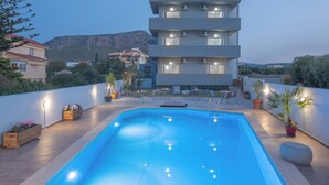 Un edificio moderno con piscina en la azotea, rodeado de plantas en macetas y mobiliario de exterior.
