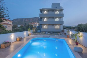 Un edificio moderno con piscina en la azotea, rodeado de plantas en macetas y mobiliario de exterior.