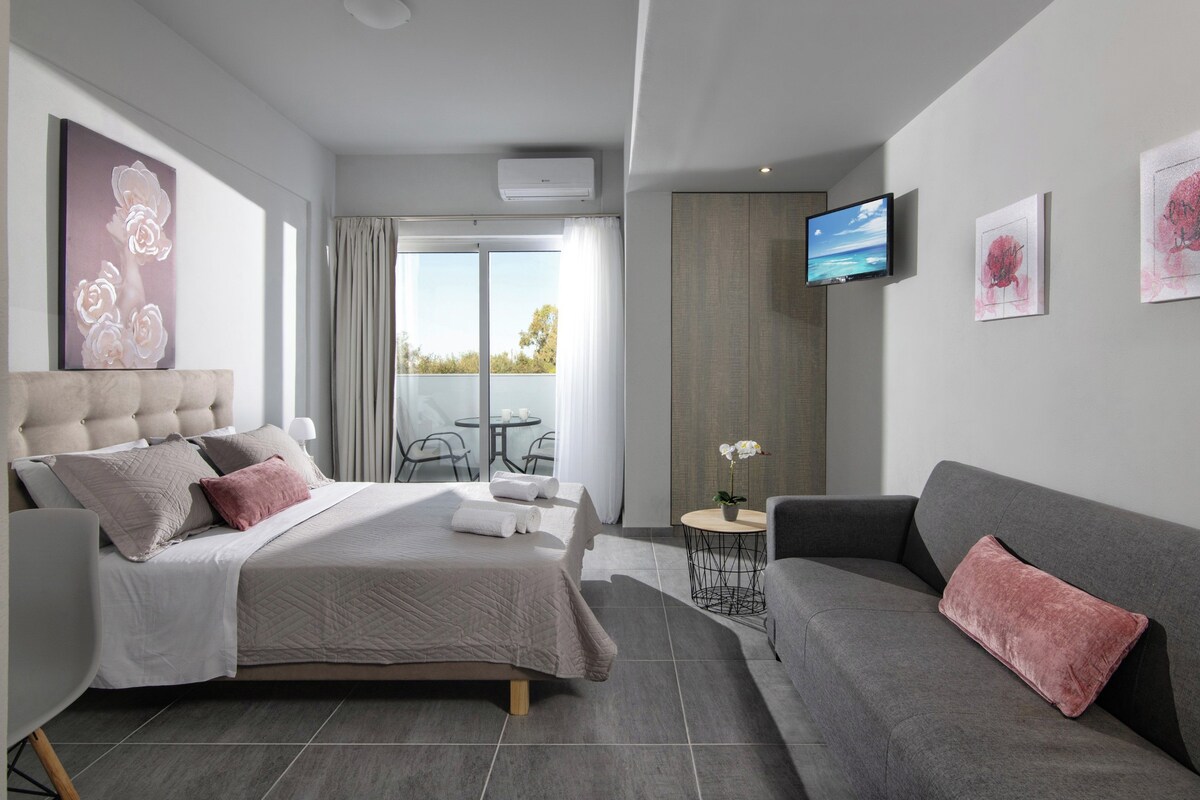 A modern hotel room with a bed, a sofa, a TV, and a balcony.
