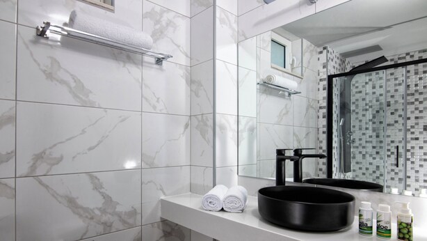 Un baño con azulejos de mármol, un lavabo negro, toallas enrolladas y artículos de aseo en la encimera.