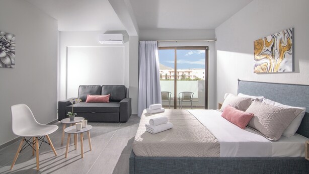 A modern hotel room with a bed, a sofa, a chair, a small table, and a balcony with a view.