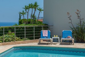 Un área junto a la piscina con dos sillas reclinables, una mesita y vistas al océano.