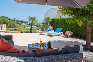 Eine Außenpatio mit Liegestühlen, einem Tisch mit Getränken und Blick aufs Meer.