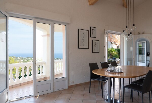 A dining area with a large table, chairs, and a view of the sea through a sliding glass door.