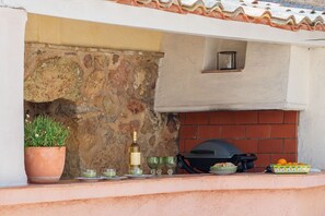 Un muro de piedra con una planta en maceta, una botella y vasos sobre un repisa.