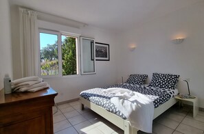 Ein Schlafzimmer mit Bett, Schminktisch, Nachttisch, Fenster mit Vorhängen und einem gerahmten Bild an der Wand.