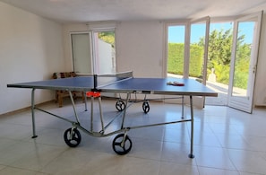 A ping pong table in a room with a sliding glass door leading to a garden. - Villa La Belle Issambre – Luxury family villa on the Côte d’Azur with sea view, heatable pool and access to nature reserve (Les Issambres)