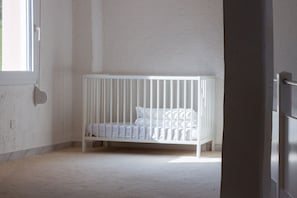 Ein weißes Babybett in einem Zimmer mit schlichter Wand und Fenster.