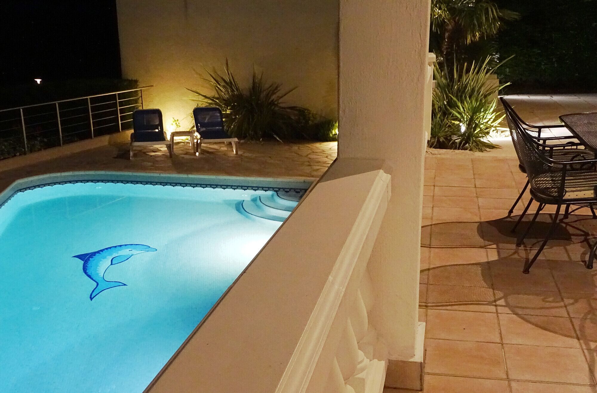 A swimming pool with a dolphin decal, lounge chairs, and a patio area with a table and chairs.