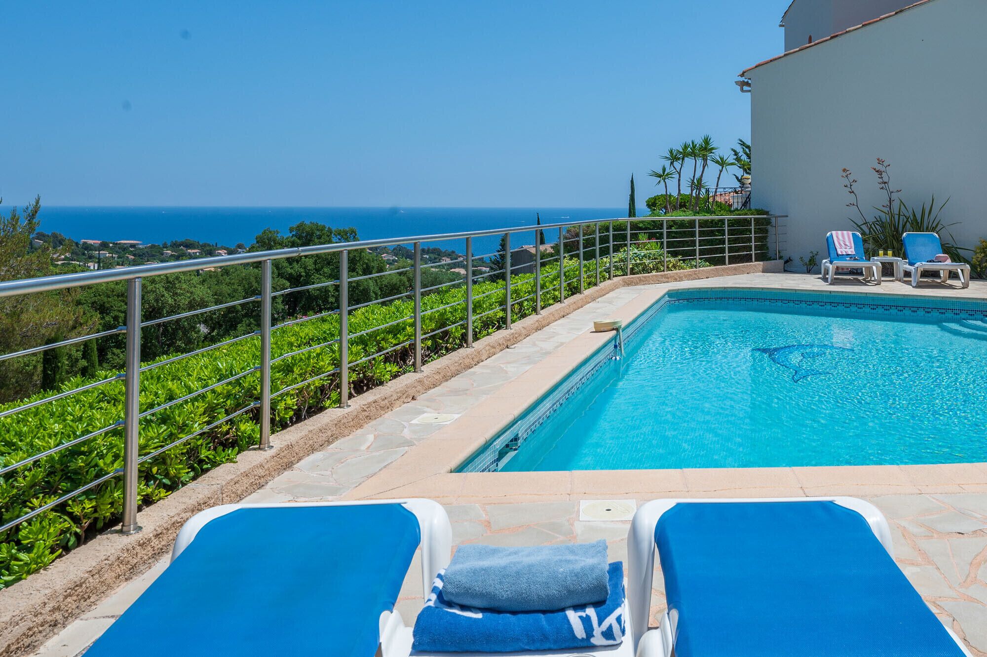 Un espace piscine comprenant deux chaises longues, une vue sur la mer et une rambarde en métal.