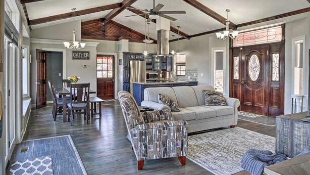 A spacious living room with a high ceiling, exposed beams, a large sofa, a dining area, and a kitchen. - Pet-Friendly Branson Area Home: Hot Tub, Game Room (Reeds Spring)