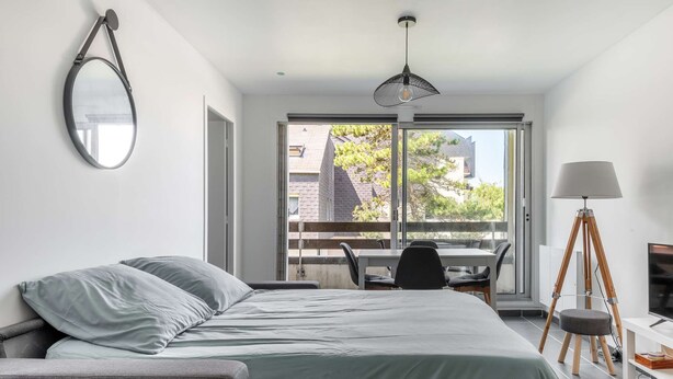 Un dormitorio moderno con cama, escritorio y silla. Una ventana grande ofrece vistas al exterior.