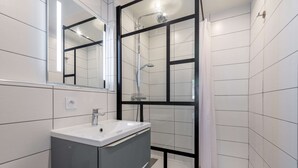 Un baño moderno con un lavamanos blanco, un espejo y una zona de ducha.