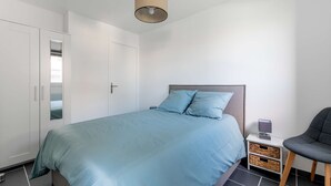 Un dormitorio con cama, armario, mesita de noche, una silla y una lámpara.