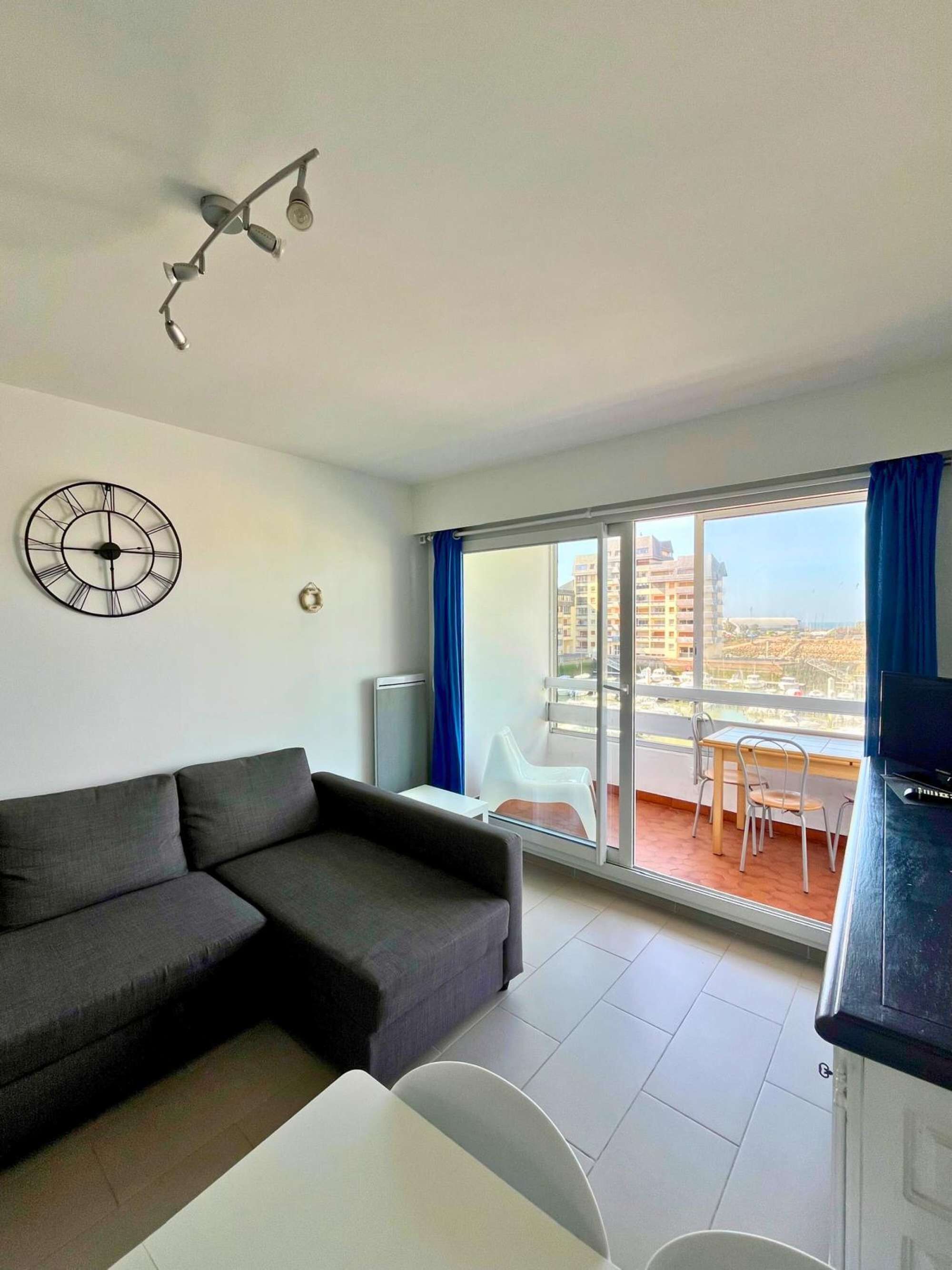 A modern living room with a grey sofa, a white table, and a large window with a view of buildings.