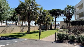 A parking area with a clear sky, palm trees, and a building with balconies.