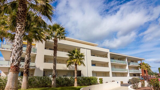 A multi-story hotel with a flat roof, surrounded by palm trees and a well-maintained lawn.