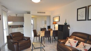 A modern living room with a brown leather sofa, a glass coffee table, and a dining area with a table and chairs.