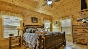 Ein Schlafzimmer in einer Holzhütte mit einem Bett, Nachttischen, einer Kommode und einem Deckenventilator.