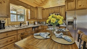 Ein Interieur einer Holzhütte mit einer Küche, die einen Edelstahlkühlschrank, Holzschränke, eine Granitabdeckung und einen Essbereich mit einem Tisch für zwei Personen zeigt.