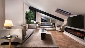 Een moderne woonkamer met een bank, fauteuil, salontafel, televisie, open haard en een plant.