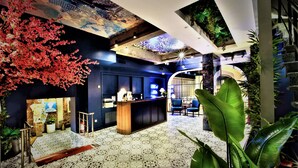 Een modern interieur met een receptiebalie, zithoek en decoratieve elementen zoals een grote plant en een muurschildering.