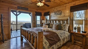 Quarto de cabana de madeira com cama, ventoinha no teto, janela com vista e um letreiro na parede.