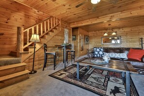 A wooden cabin interior with a staircase, a sofa, a coffee table, and a patterned rug. - Above & Beyond Lodge | Blue Ridge, Ga (Blue Ridge)