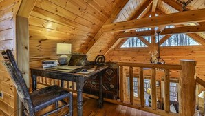 Interior de uma cabana de madeira com uma escrivaninha, cadeira e vista pela janela.