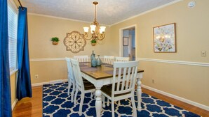A dining room with a wooden table, white chairs, a chandelier, and a blue patterned rug. - Relax at the serene and spacious duplex nestled in the peaceful, family-friendly neighborhood. (Johnson City)
