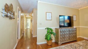 A hallway with wooden flooring, a television on a cabinet, and a plant. - Relax at the serene and spacious duplex nestled in the peaceful, family-friendly neighborhood. (Johnson City)