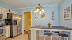 A kitchen with a stainless steel refrigerator, a built-in oven, a sink, and a bar area with stools. There is a ceiling light fixture above the bar. - Relax at the serene and spacious duplex nestled in the peaceful, family-friendly neighborhood. (Johnson City)