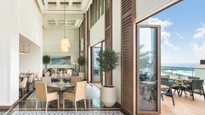 A spacious dining area with a large table and chairs, a potted plant, and a view of the ocean through large sliding doors. - Address Beach Resort Fujairah (Al Aqah)